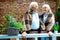 Pensioners smiling while standing in plaid blankets near flower pots