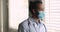 Pensive African male doctor wear uniform facemask looking out window