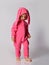 Pensive barefoot cute blonde baby girl in pink warm jumpsuit with hood and bunny ear walks slowly looking down