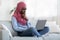 Pensive black muslim female freelancer with laptop at home brainstorming at project
