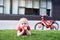 Pensive blond boy is resting on the lawn. Bike in the background