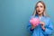 pensive blond girl holding a piggy bank with a stock thinks where to spend money on a blue isolated background