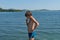 A pensive boy of 11 years old stands on the beach, against the background of a blue large lake on a summer sunny day