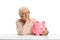 Pensive elderly woman with a piggybank seated at a table