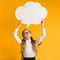 Pensive Elementary School Girl Holding Speech Bubble Overhead, Yellow Background