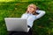 Pensive girl in glasses lying on the grass in the park with a laptop computer, dreams of something