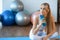 Pensive girl in sportswear sitting on the floor in the gym with sports bottle in her hand.