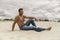 Pensive handsome young man sitting on the dunes in desert