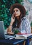 Pensive hipster girl in trendy hat sitting at table on street cafe talking on mobile phone