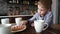 A pensive little boy sits at a table with a circley tea and cakes. Licking his finger. Portrait.