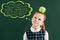 pensive little red haired schoolgirl with apple on head standing near chalkboard with words on different languages