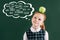 pensive little red haired schoolgirl with apple on head standing near chalkboard with words of different professions