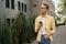 Pensive man wearing yellow casual shirt and stylish eyeglasses using mobile phone walking on the street, copy space