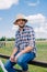 pensive middle aged farmer in panama hat sitting on fence and looking away