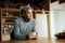 Pensive multi-cultural elderly male, leaning on kitchen counter with coffee mug in modern kitchen.