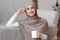 Pensive muslim girl in hijab relaxing with tea at home