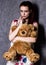 Pensive or offended beautiful woman embraces a teddy bear on a gray background.