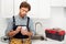 Pensive plumber using smartphone near toolbox