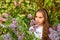 Pensive portrait of a teenage girl in lilac bushes in a white dress