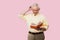 pensive senior man touching grey hair and reading book isolated on pink.