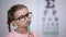 Pensive smart girl wearing glasses, testing vision with eye chart in clinic