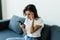 Pensive stressed young woman sit on sofa at home using cellphone look in distance pondering of problem. Anxious female feel