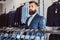 Pensive tattoed male with stylish beard and hair dressed in elegant suit standing in a menswear store.