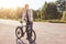 Pensive teenage boy standing on road, keeping hand on handle bar of his bike, waiting for others cyclists to have journey together