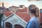 Pensive thoughtful woman tourist looking at beautiful cityscape of old Europe town with orange tile roofs at sunset during travel