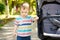 Pensive toddler boy stands near the stroller in the park. Cute kid of one and a half years. Selective focus