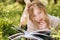 Pensive woman lying on grass and reading magazine