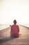 Pensive woman tourist sitting on wooden pier at beach during sunset and looking at infinity view towards horizon and sunset sky