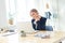 Pensive young beautiful businesswoman working on laptop and keeping hand on chin while sitting at her workplace