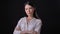 Pensive young brunette woman in shirt with crossed hands thinking and standing isolated on black background