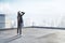 Pensive young businesswoman standing on building roof on beautiful sky background with mock up place for your advertisement.