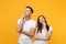 Pensive young couple two friends guy girl in white empty blank t-shirts posing isolated on yellow orange background