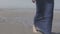 Pensive young woman in denim jacket walking on lonely beach.