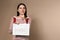 Pensive young woman holding calendar with marked menstrual cycle days on beige background