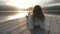 Pensive young woman with long hair seen from behind looks at the lake at sunset lying on an old wooden pier