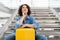 Pensive Young Woman Sitting With Suitcase On Stairs In Airport