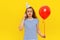 Pensive young woman is talking on a mobile phone, holds red inflated helium balloon, celebrates birthday or special occasion,