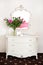 Peony flowers on a white commode under a mirror