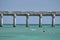 People bathing in sea clear blue water under long pier bridge on hot summer day