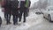 People cross the road at a pedestrian crossing in winter. Snowflakes fall slowly