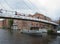 People crossing the footbridge at calls landing leeds with a boat sailing along the river past waterfront buildings