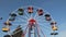People enjoy riding an old retro ferris wheel in amusement park against a blue sky.