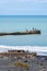 People fishing on end of breakwater beyond shipwreck in beach. Patea coastal landscape