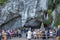 People in front of grotto of Sanctuary of Our Lady in Lourdes, France. Grotto of Our Lady with pilgrims on benches.