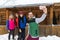 People Group Taking Selfie Photo On Smart Phone Near Wooden Country House Winter Snow Resort Cottage