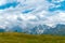 People, hikers walk far in the long distance, on a summer sunny day, against the background of snow-capped peaks of the Caucasus